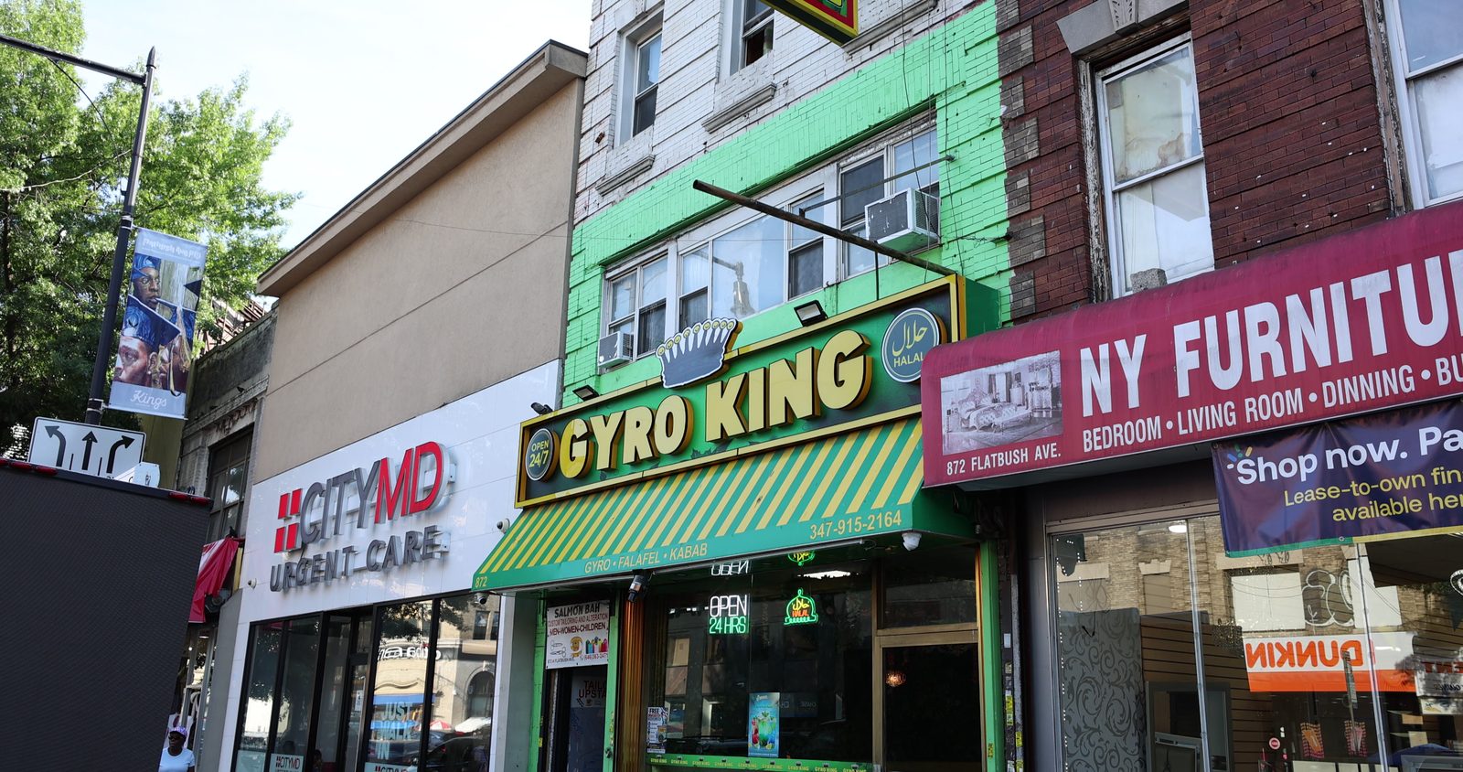 The Gyro King storefront on Flatbush Avenue in Brooklyn, between an urgent care and a furniture store, with its green-and-yellow awning and sign